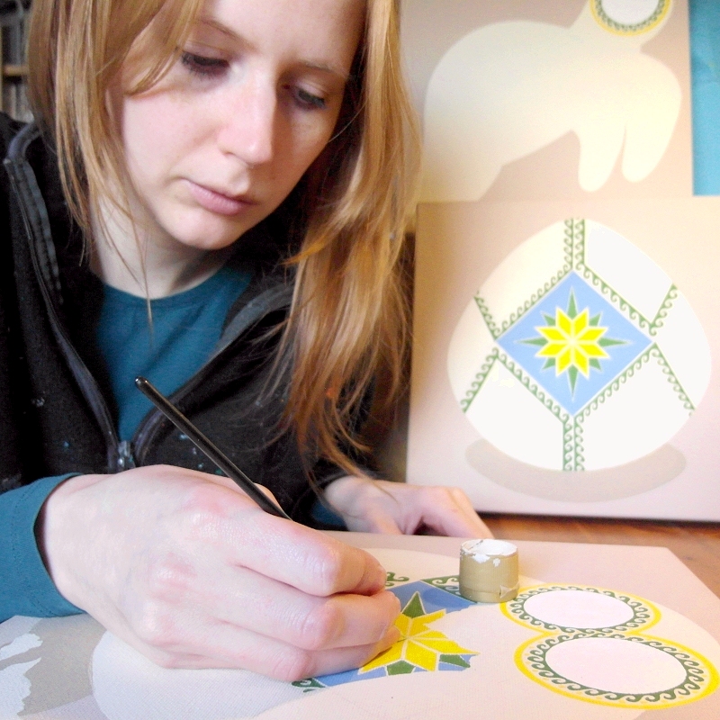 Kim Onyskiw painting on a half complete canvas, with two other partially painted canvases in the background