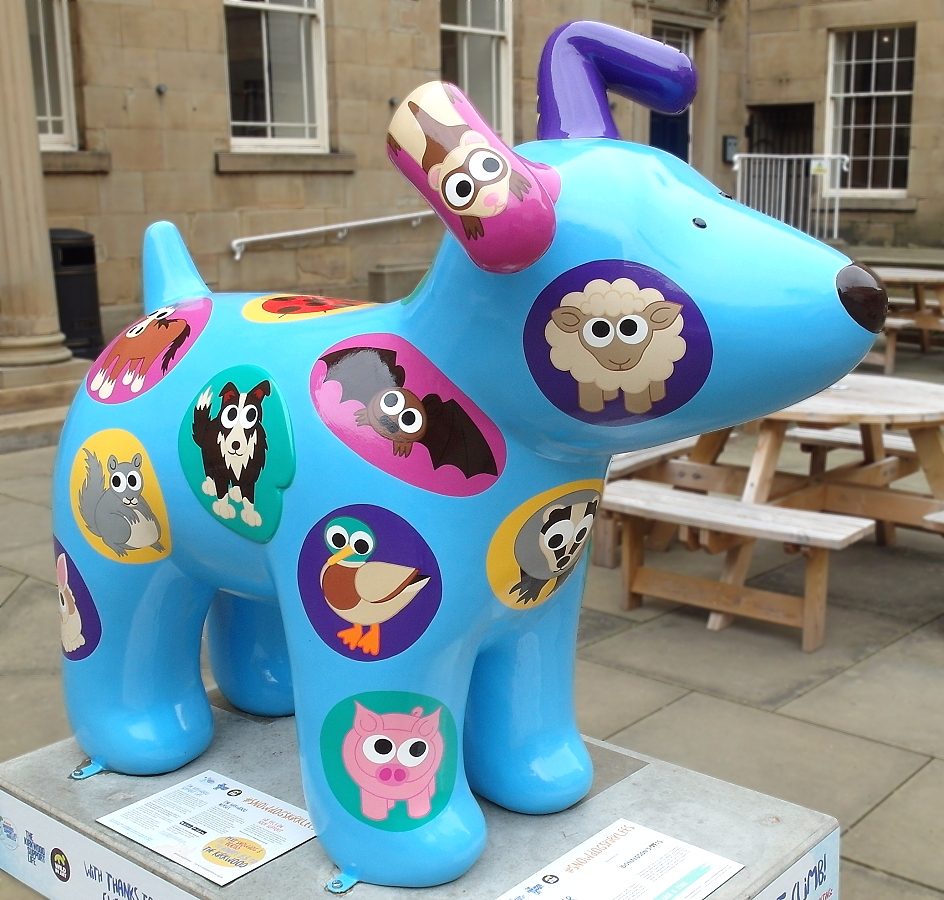 A large blue fibreglass sculpture of a dog covered in colourful patches, each with a cartoon animal painted on